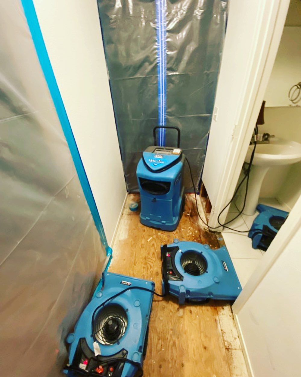 A bathroom with two blue vacuums on the floor, being cleaned by water damage remediation experts.