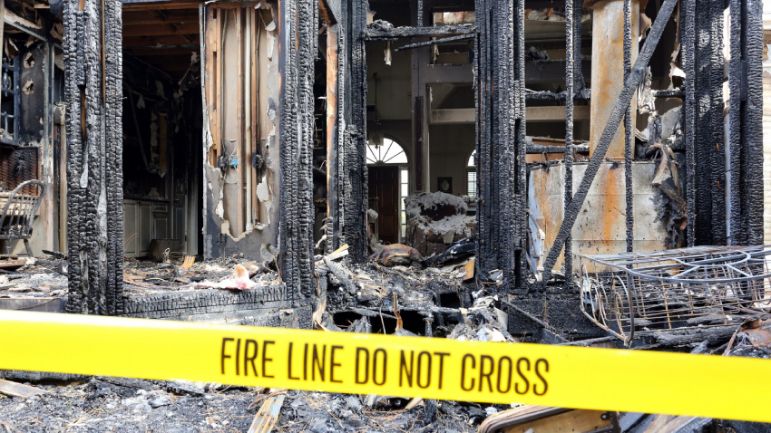 The remains of a home after a fire with a “Fire Line Do Not Cross” sign marking it. The remains of a home after a fire with a “Fire Line Do Not Cross” sign marking it.