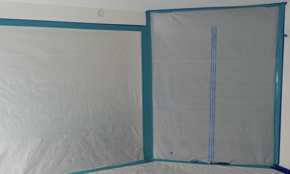 A room with plastic sheeting and tape on the floor, being prepared for fire damage remediation by Bravo Restoration.