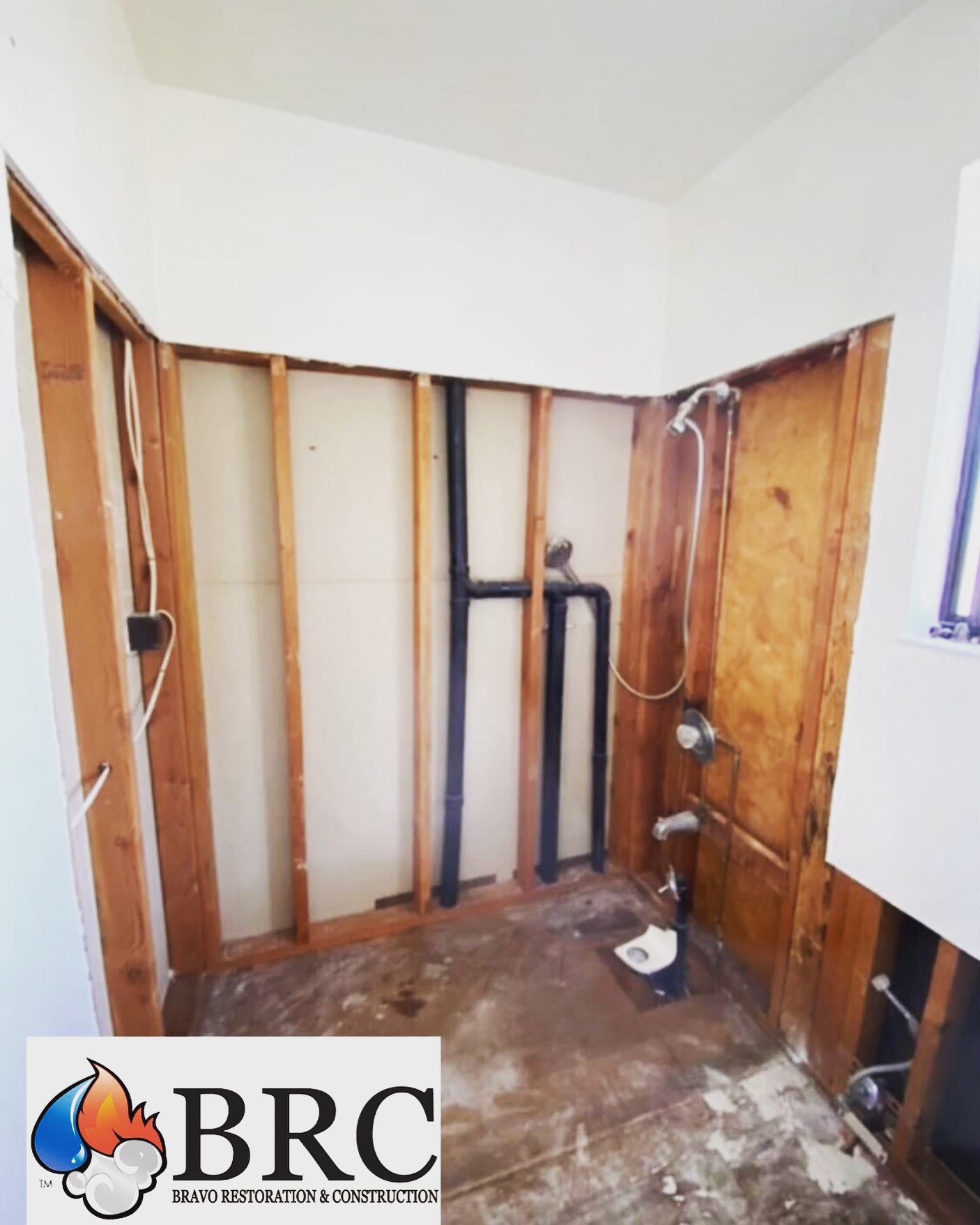 A stripped-down room under renovation with exposed wooden studs and plumbing, showcasing the early stages of water damage restoration. The Bravo Restoration & Construction (BRC) logo is in the bottom left corner.