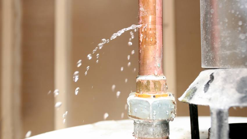 A copper pipe with a pinhole leak sprays water into a home.