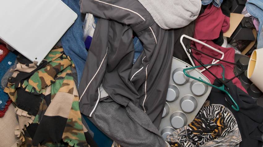 A very dirty room in a hoarding house with clothes, dishes, and more.