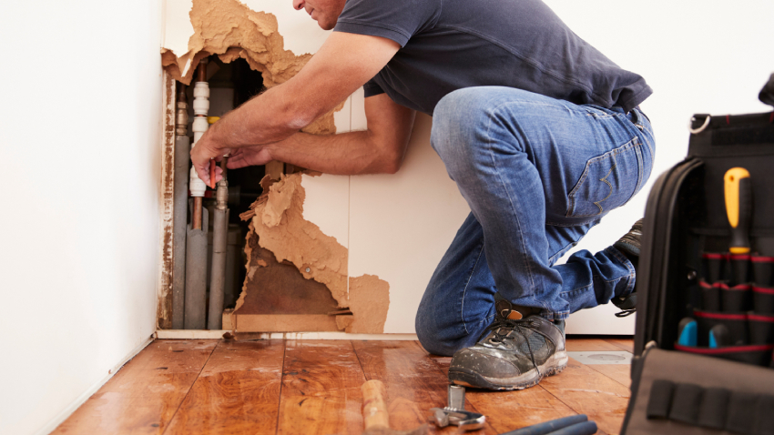 A licensed contractor fixes a pipe behind a wall where water damage was found.